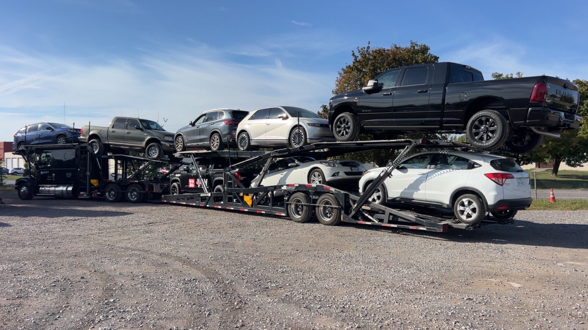 Allstar Hauling nine-car carrier fully loaded with pickups, SUVs and sedans on a gravel staging lot