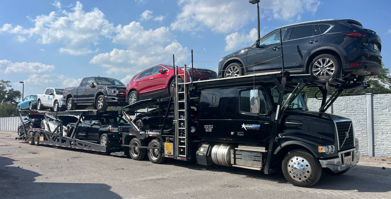 Black Allstar Hauling Volvo VNL eight-car carrier fully loaded with trucks, SUVs and sedans under a blue sky